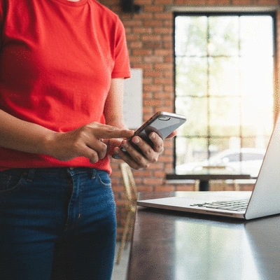 Person using a smartphone and laptop simultaneously in a bright cafe